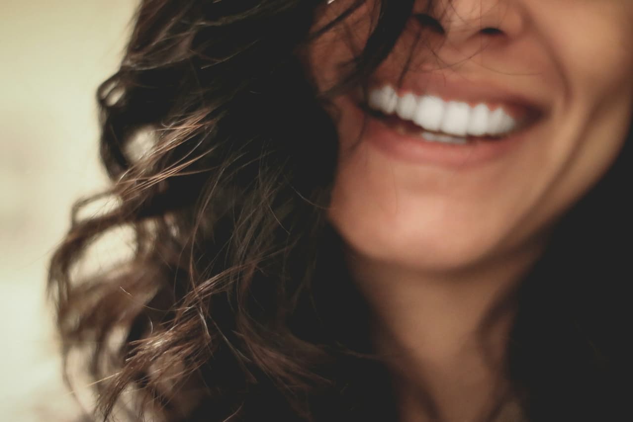 Mulher sorrindo em close, com cabelos ondulados e luz natural quente