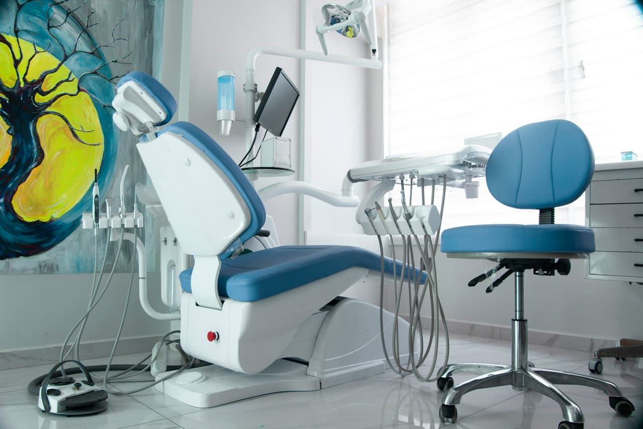Consultório com cadeira odontológica azul e painel artístico na parede
