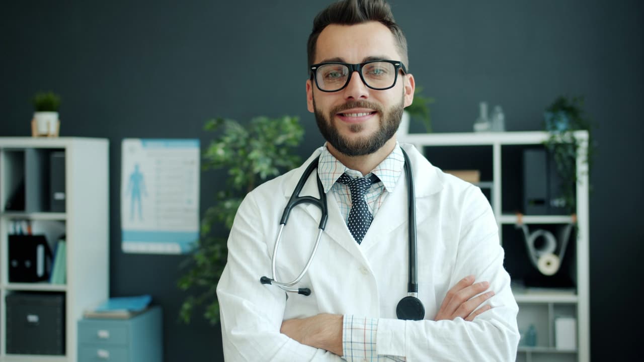 Dentista de óculos e estetoscópio, de braços cruzados, sorrindo