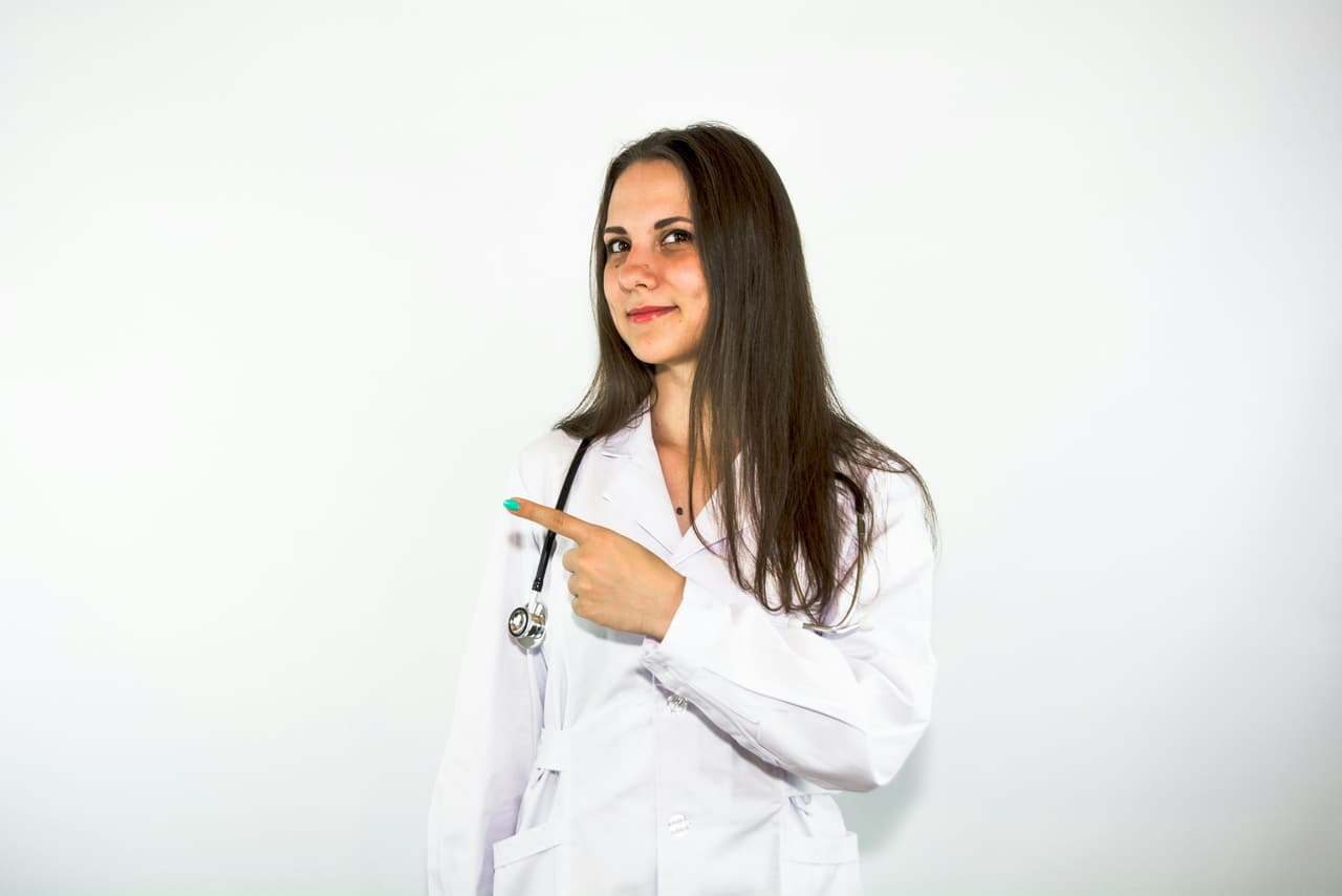 Dentista de jaleco branco apontando para o lado, sobre fundo claro